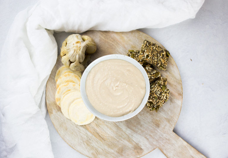 White bean dip on brown board, with white background.