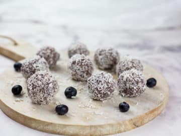 Close up of blueberry and cacao vegan energy balls on chopping board on a marble background