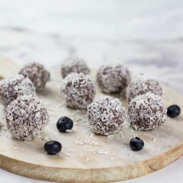 Close up of blueberry and cacao vegan energy balls on chopping board on a marble background