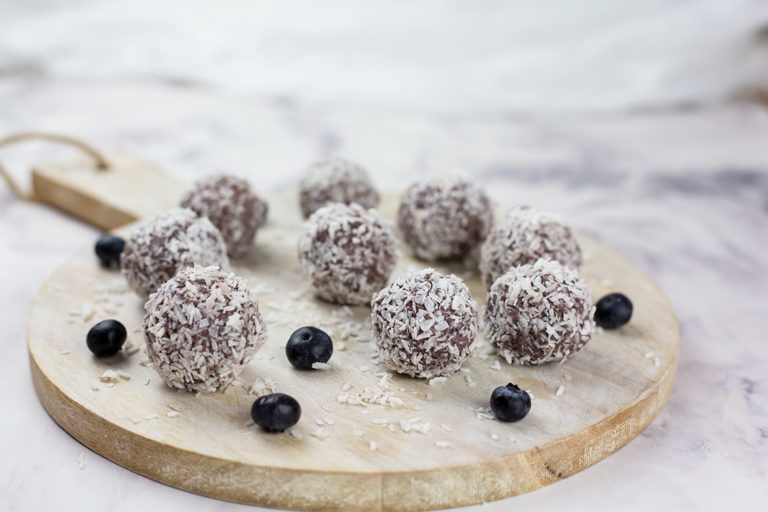 Close up of blueberry and cacao vegan energy balls on chopping board on a marble background