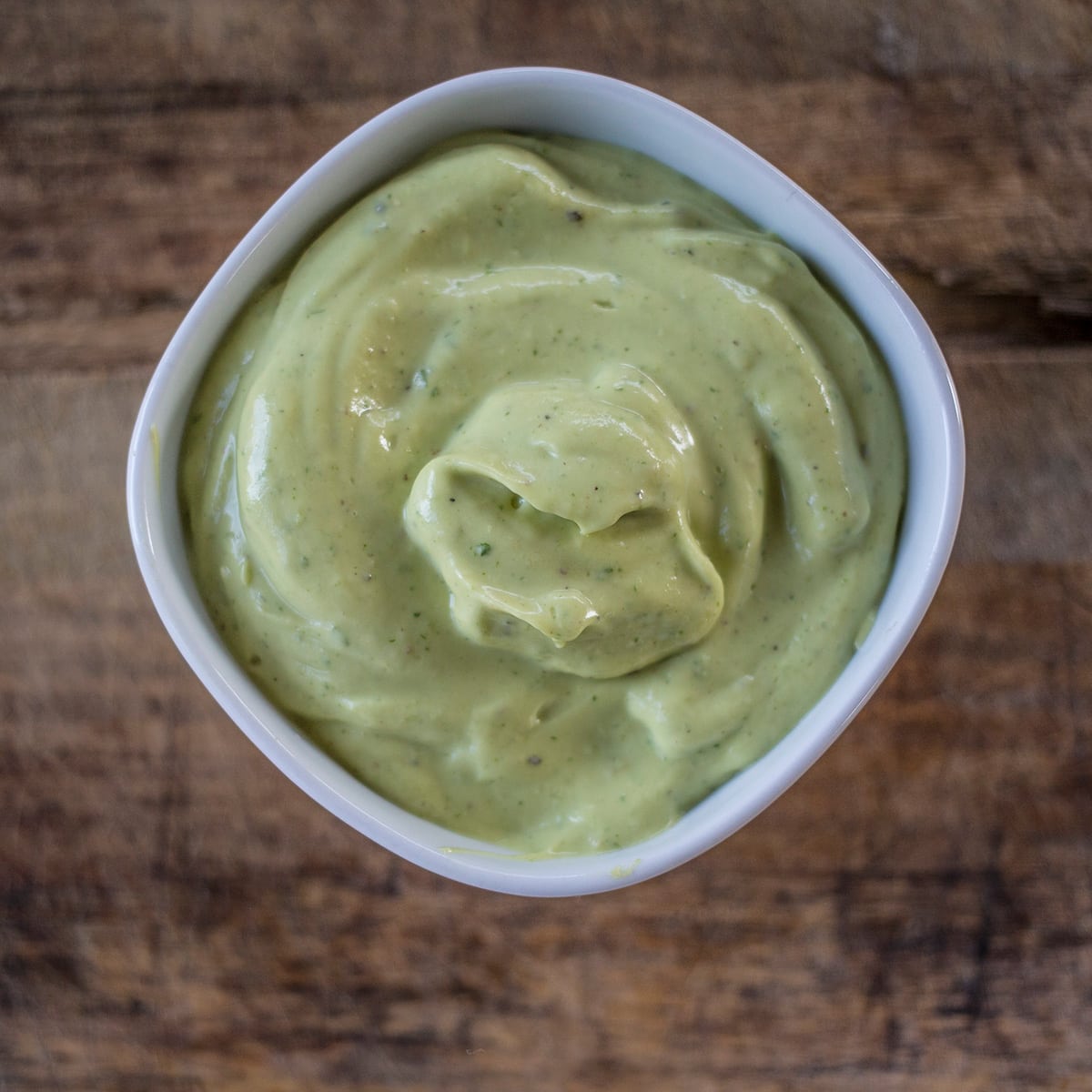 Avocado sauce in white bowl on wooden backrgound.