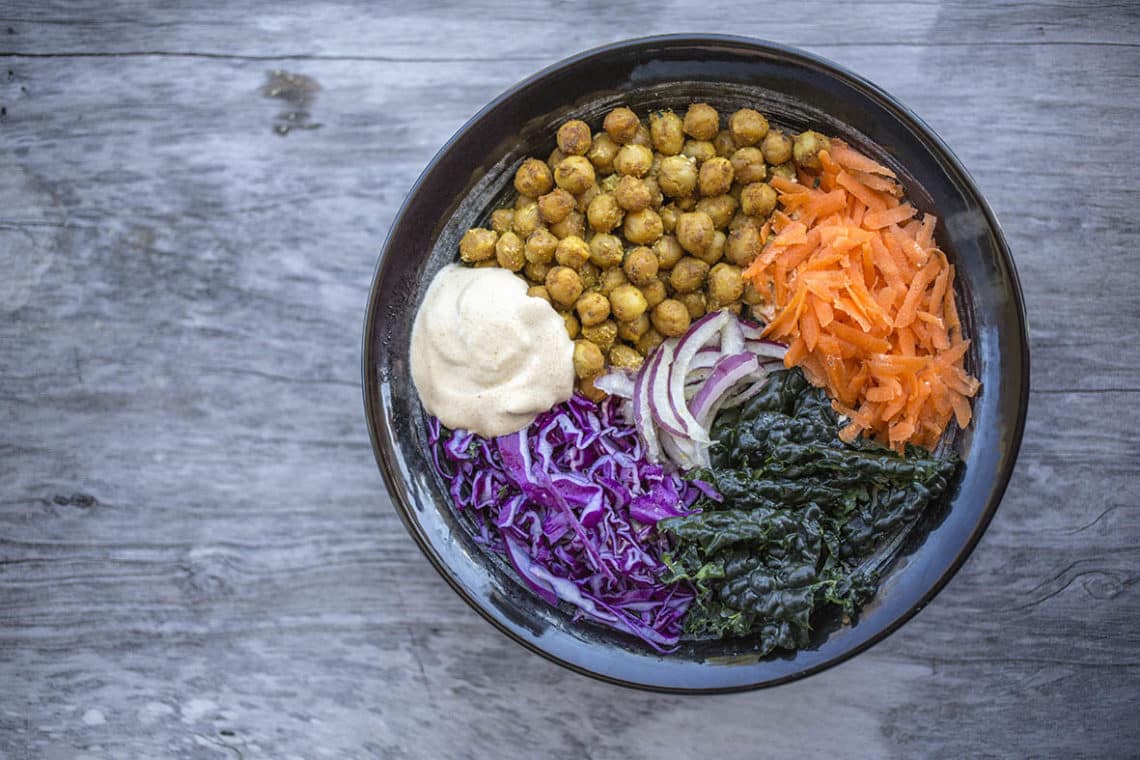Birds eye view of spicy chickpea buddha bowl in black bowl on a wooden background.