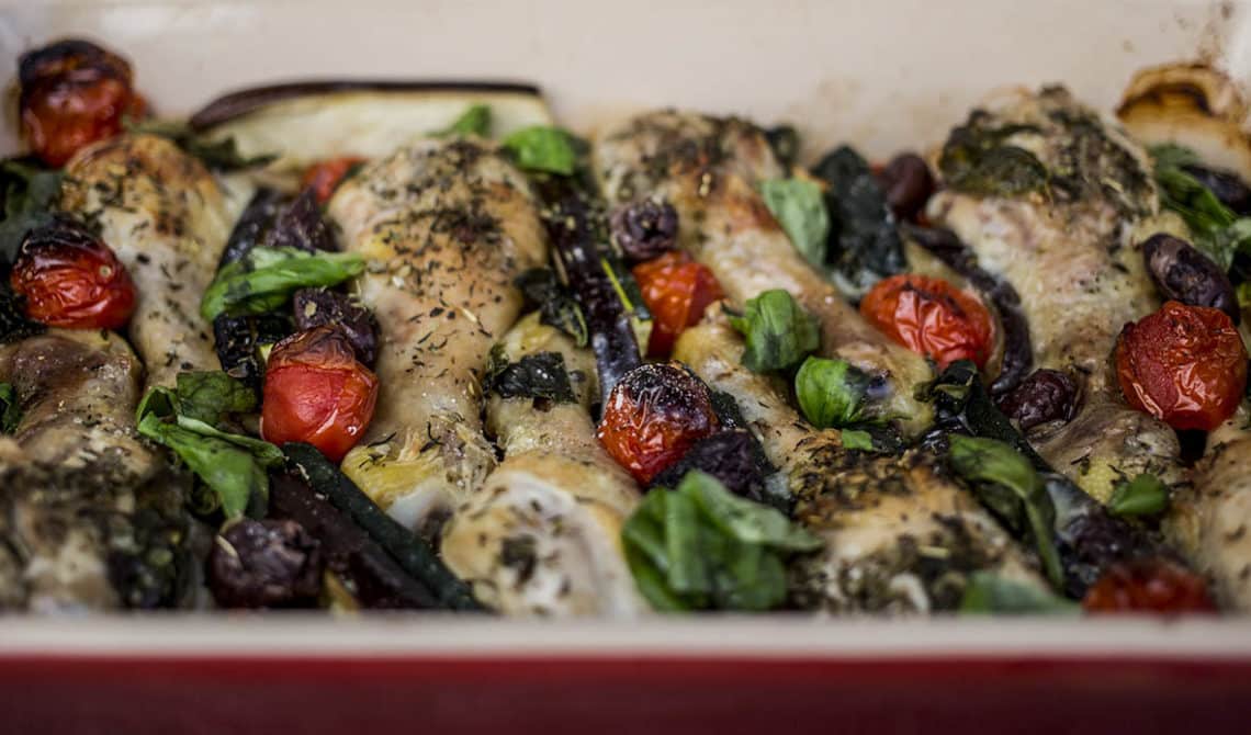 Meditteranean Chicken Bake close up with drumsticks in a red baking dish.