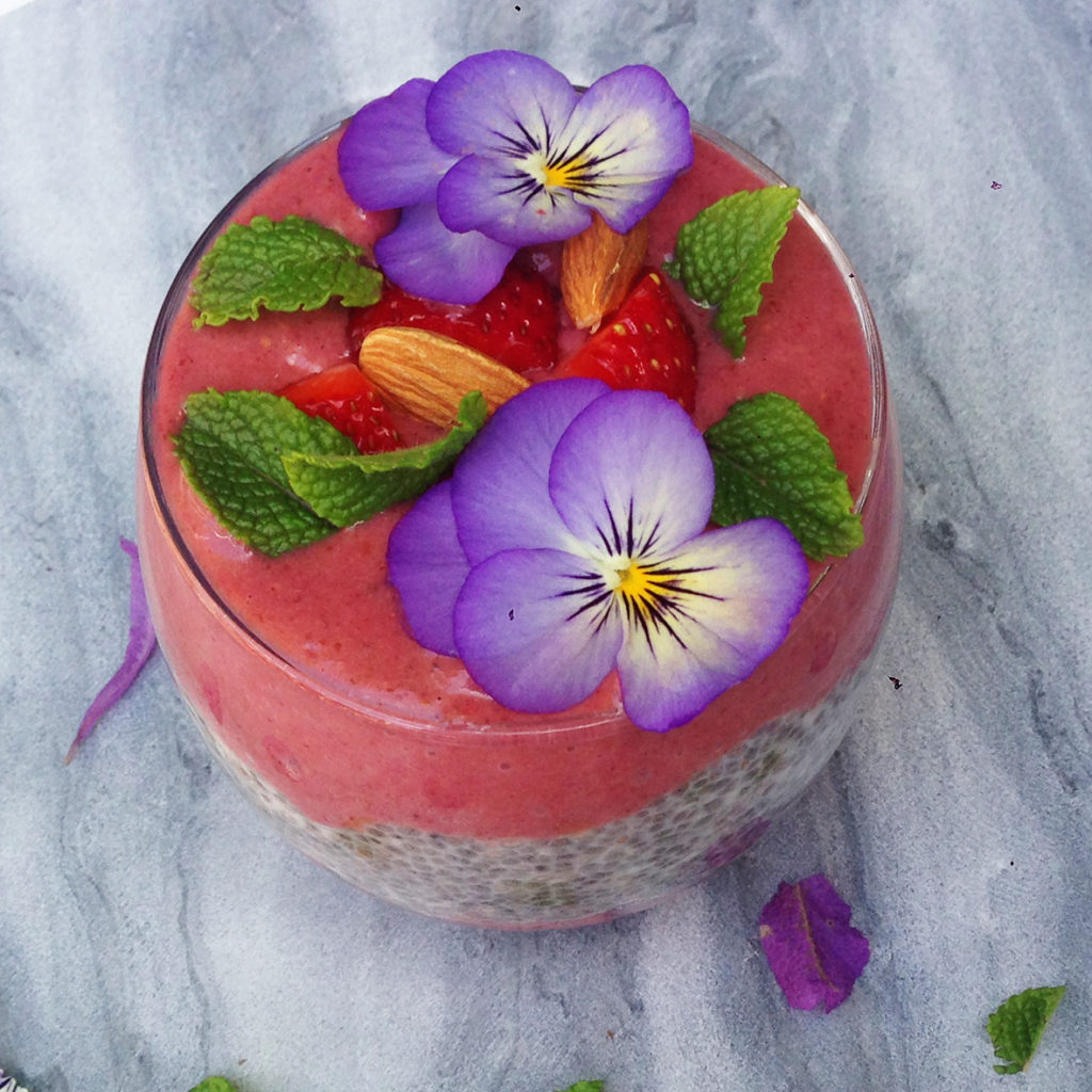 A delicious layered strawberry chia pudding with a creamy coconut chia layer, fresh strawberries & a smooth strawberry, acai & banana layer. On a marble background.