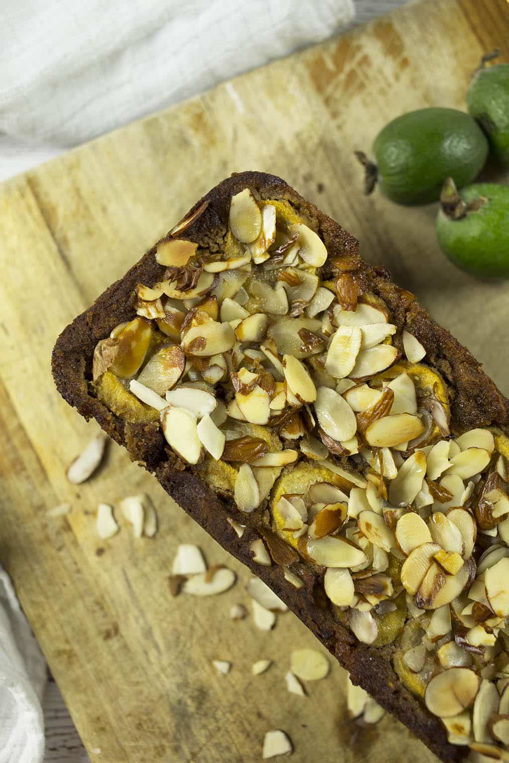 Close up of Feijoa and Banana Bread with sliced almonds on top on chopping board.