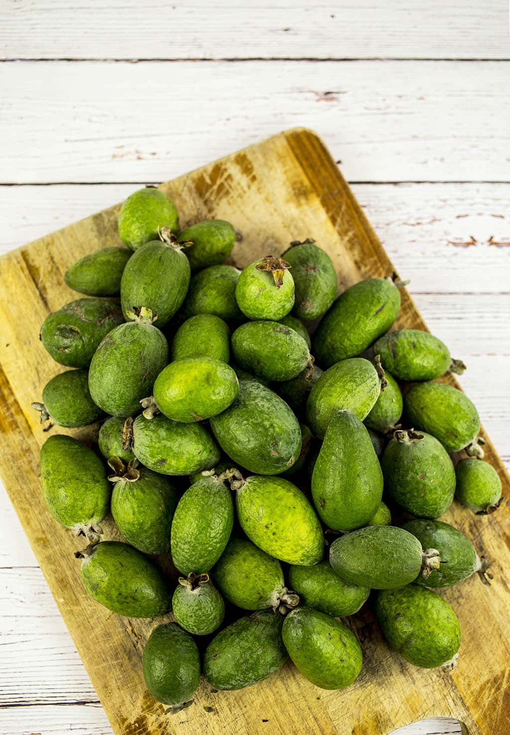 Feijoas on chopping board on white background.