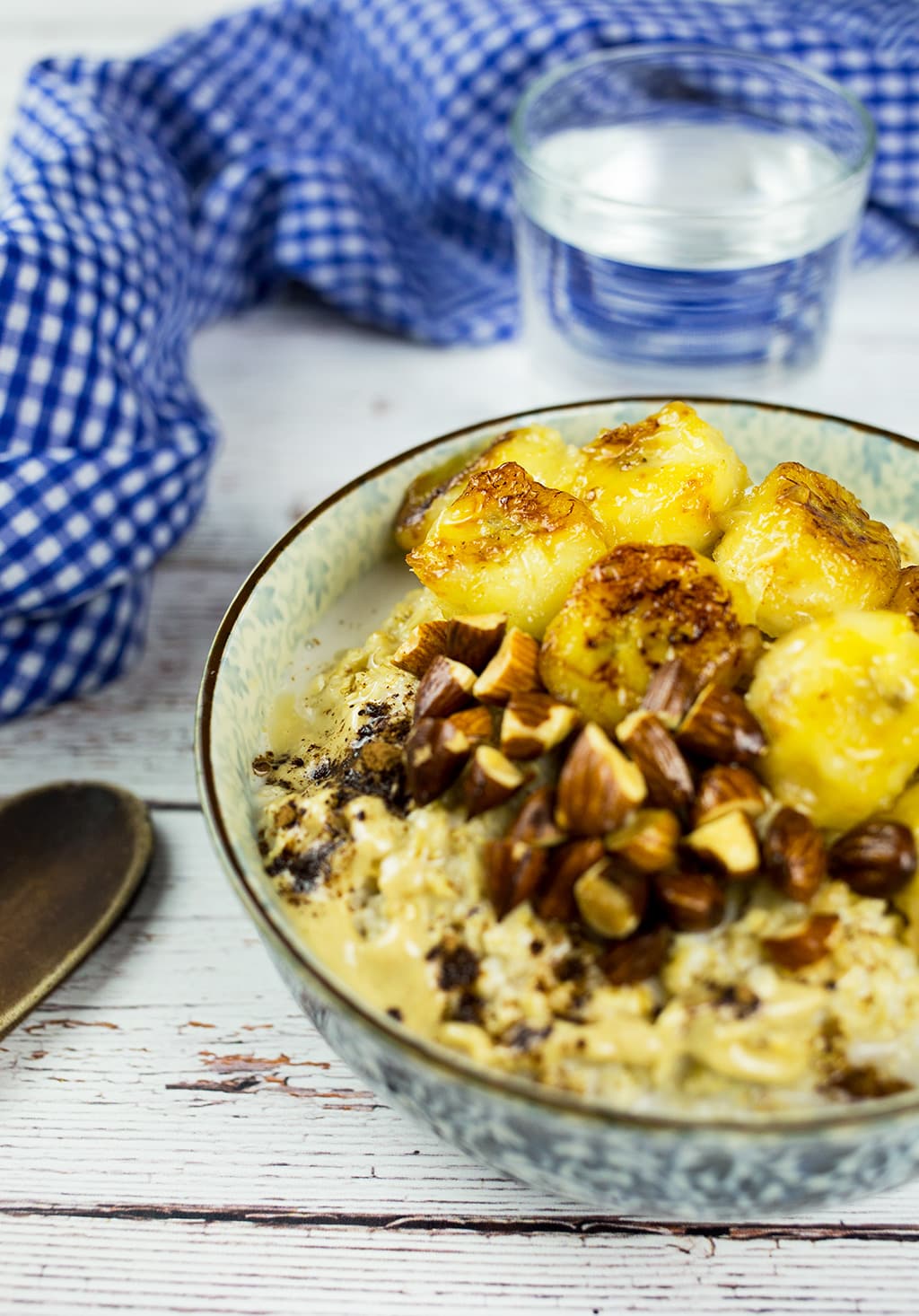 Tahini Oatmeal with Caramelized Bananas with water in background and wooden spoon to the left.