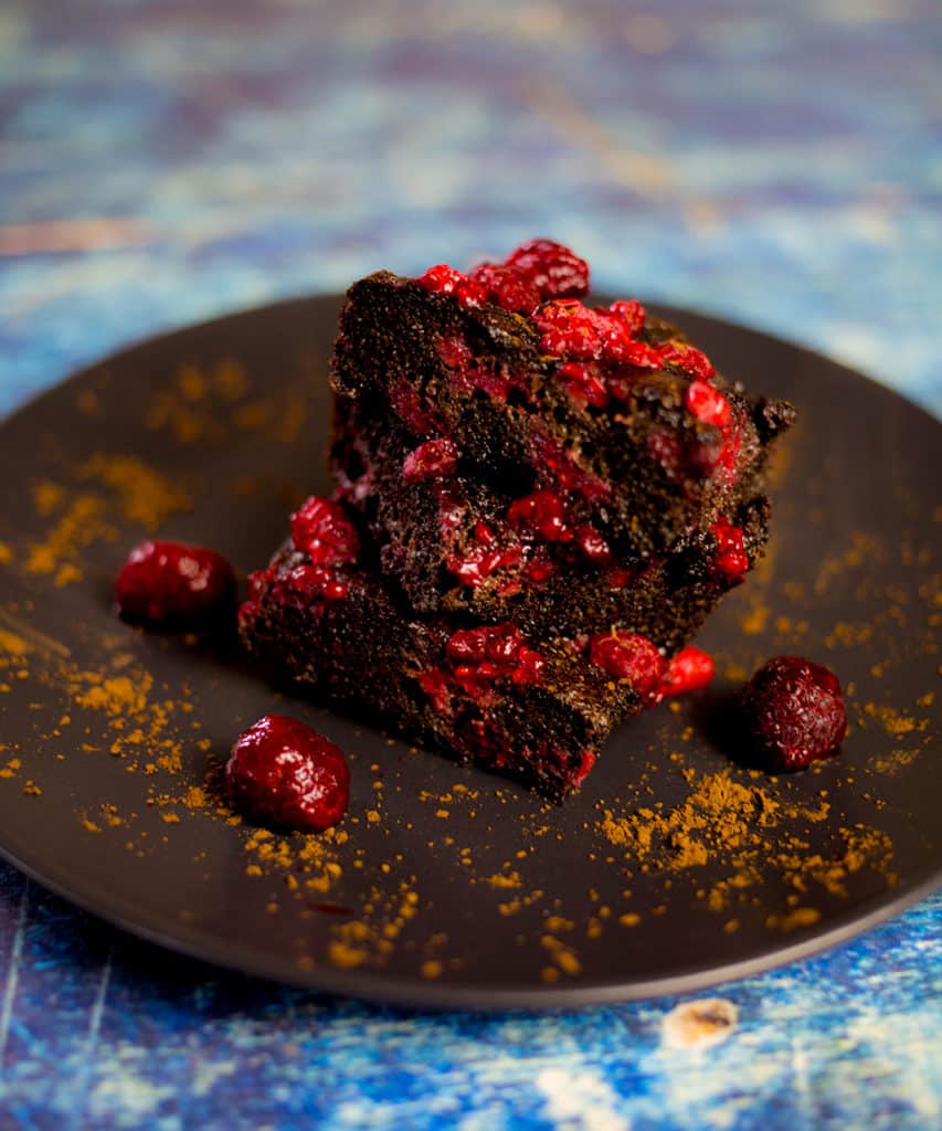 Chocolate raspberry brownies stacked on plate on blue background.