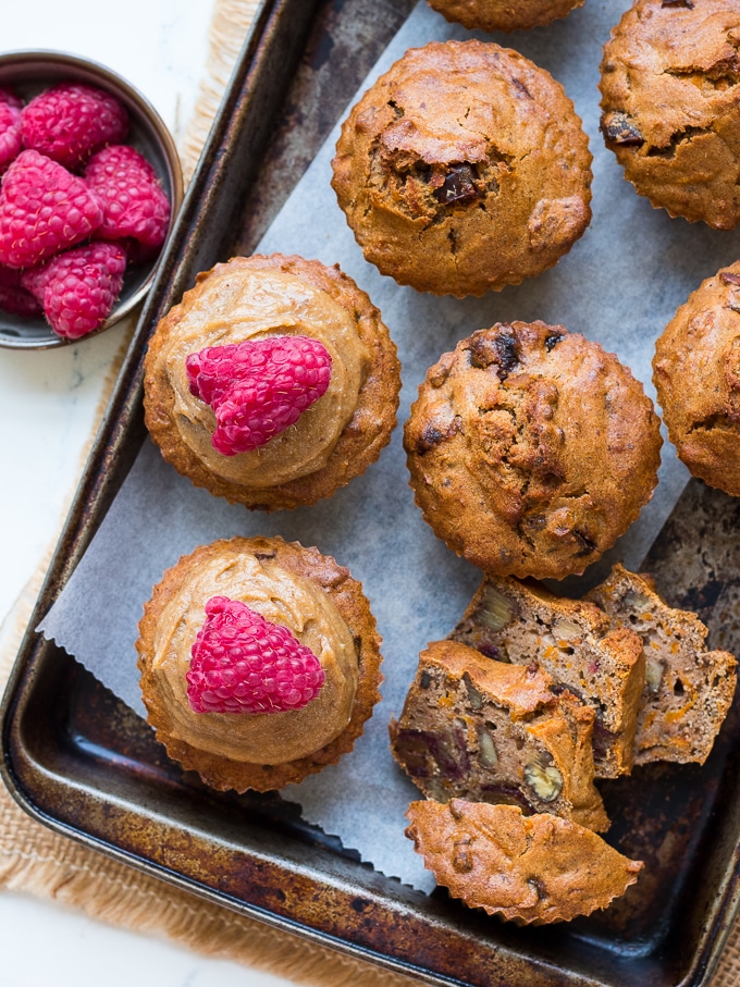 Buckwheat, carrot, date and walnut muffins on baking tray some with raspberries on top with raspberries in a bowl to the side.