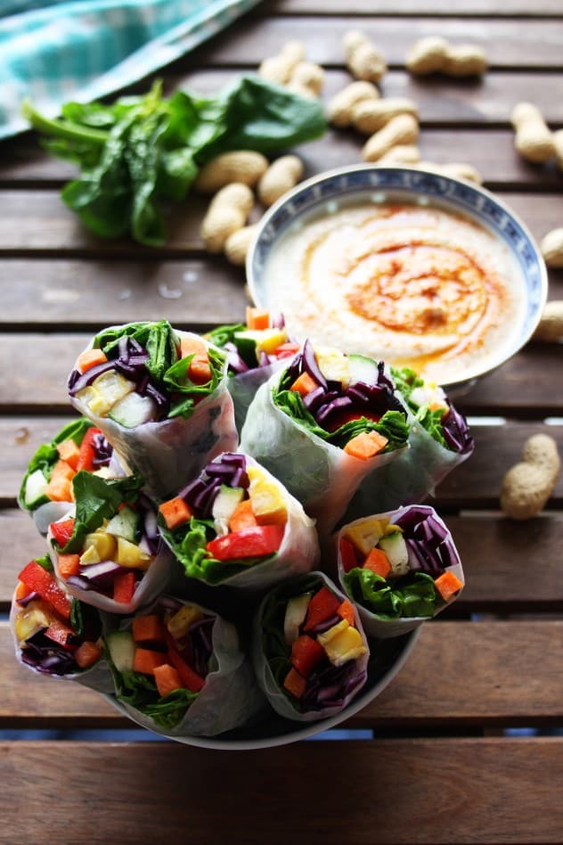 Veggie spring rolls with bowl of peanut sauve and scattered peanuts on wooden table.