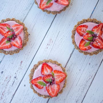 Four mini strawberry tarts on white table.