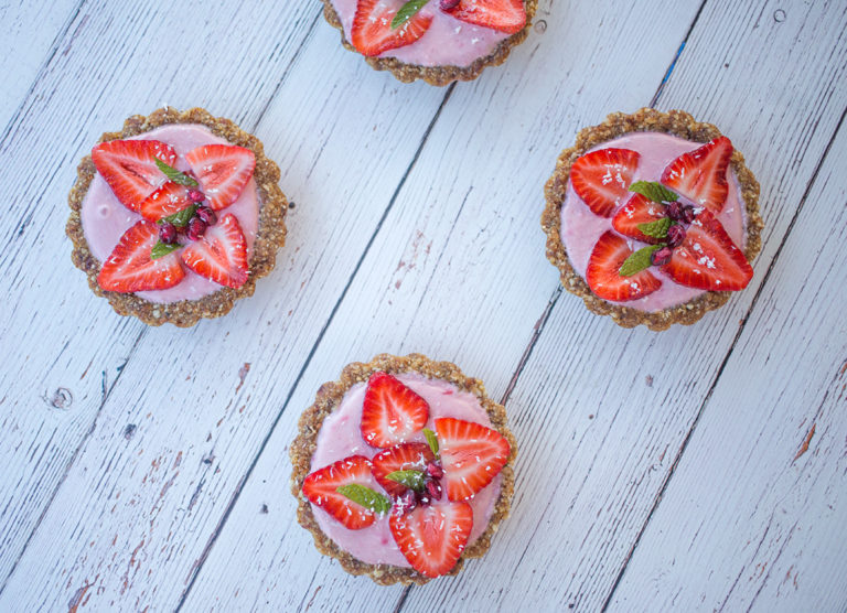 Four mini strawberry tarts on white table.