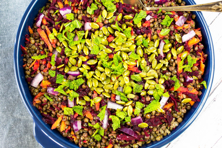Birdseye view of french lentil salad iwth mint on top in a blue bowl with a grey cloth in the background.