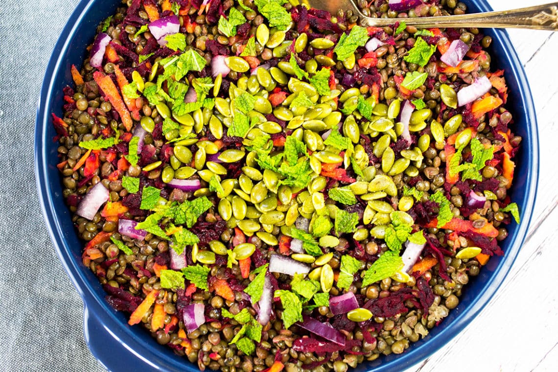 Birdseye view of french lentil salad iwth mint on top in a blue bowl with a grey cloth in the background.