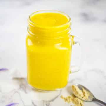 Mango Smoothie with Maca in glass with teaspoon of maca powder