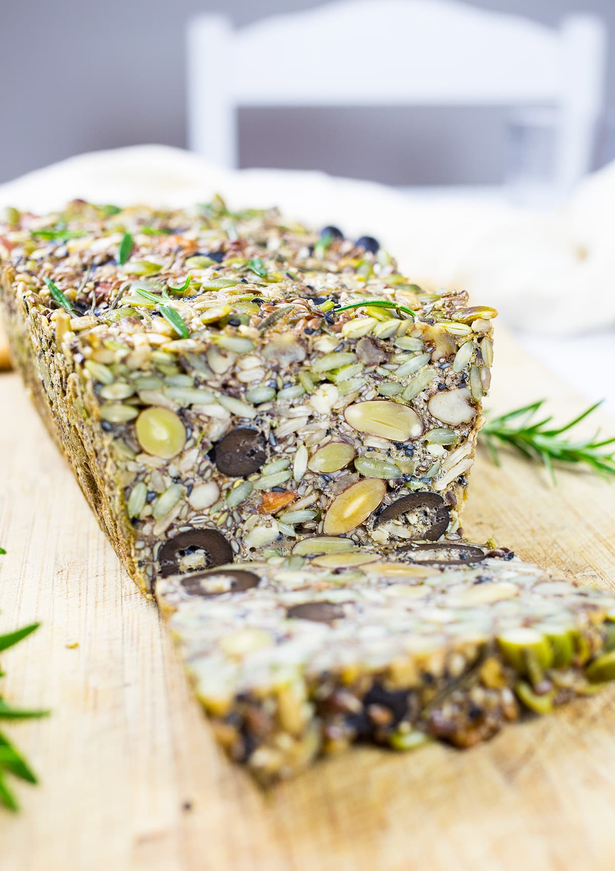 Sliced Paleo Nut Bread on chopping board with white chair in the background.