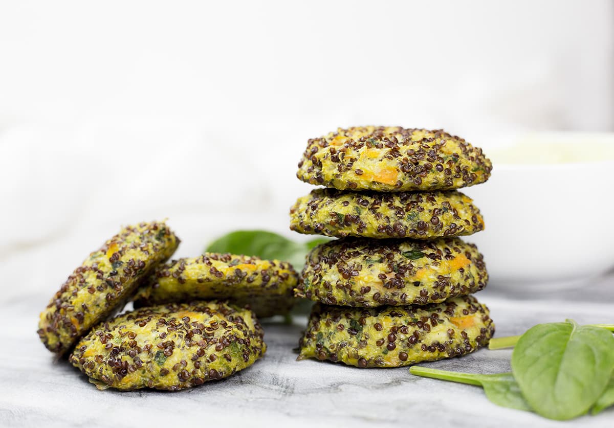 6 quinoa patties on marble background with avocado dipping sauce behind.
