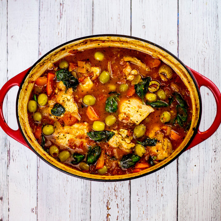 Birdseye view of Spanish chicken stew in red dish on white background.