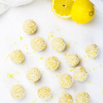 Birdsye eye view of lemon bliss balls scattered on white background with lemon in background cut in half.