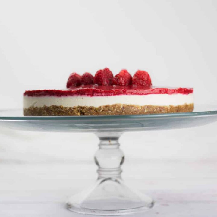 Raspberry vegan cheesecake on glass cake stand.