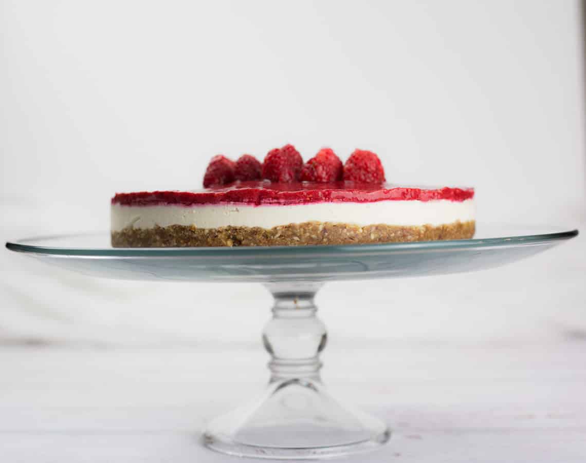 Raspberry vegan cheesecake on glass cake stand.