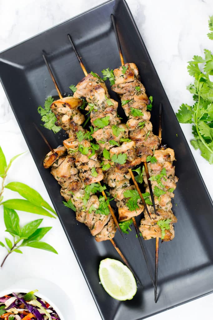 Birds eye view of chicken skewers on black platter with side salad and coriander