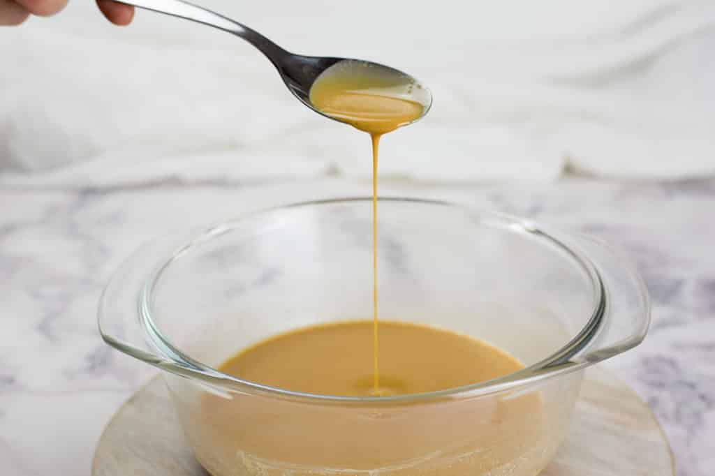 Liquid to make peanut butter fat bombs in a glass bowl, with a teaspoon dripping some peanut butter liquid into the bowl.