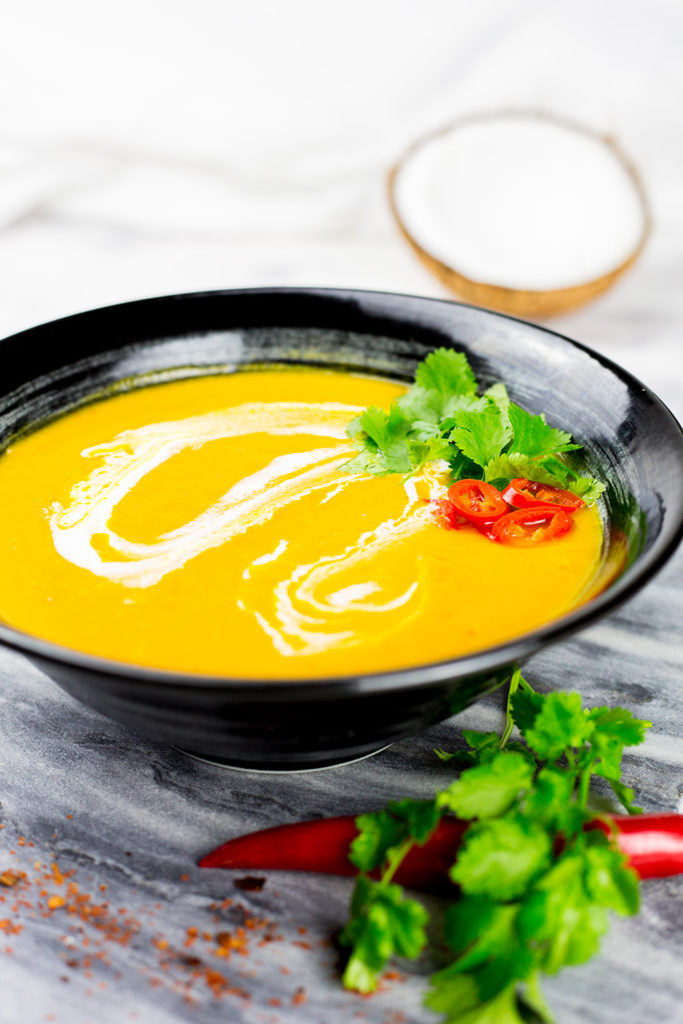 Vertical photo of Thai Butternut Squash Soup with coconut in background.