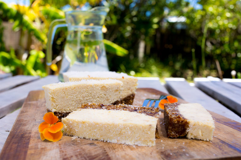Pineapple and coconut slice on wooden table with water jug behind.