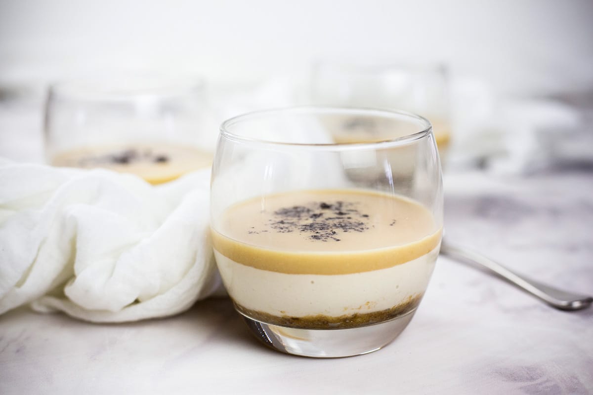 Mini salted caramel desserts in glasses with white cloth behind.