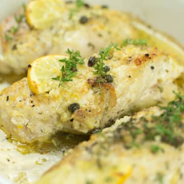 Close up of baked lemon chicken in white baking dish.