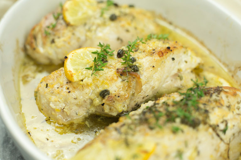 Close up of baked lemon chicken in white baking dish.