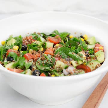 Quinoa salad in white bowl with wooden servers.
