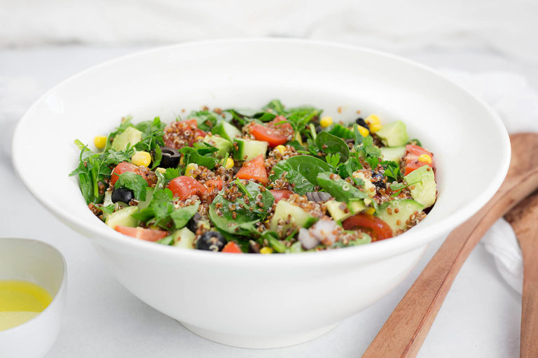 Quinoa salad in white bowl with wooden servers.