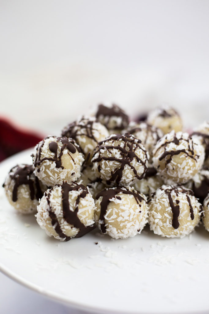 Vertical image of coconut almond snowballs on white platter with red and white background.
