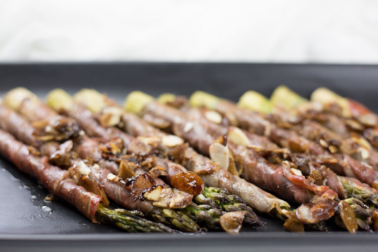 Prosciutto wrapped asparagus on black platter.