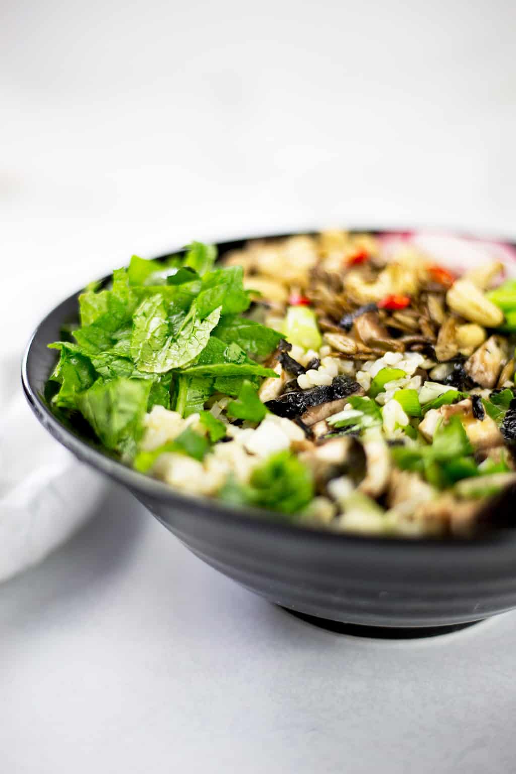 Photo showing half of the Asian buddha bowl focousing on the mushrooms and radish leaves with white cloth in background.