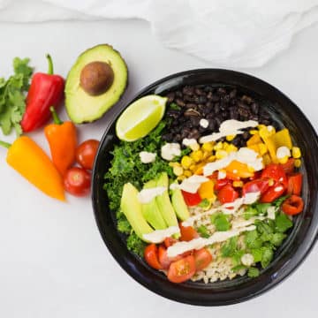 Birdseye view of vegan burrito bowl with avocado, red and orange pepper and coriander in background on a white backdrop.