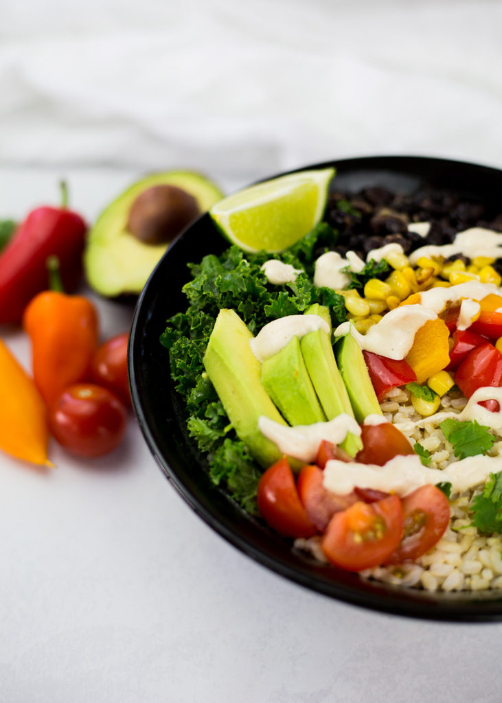 Close up of vegan burrito bowl in black bowl with dressing poured over the top and lime wedge on the side.