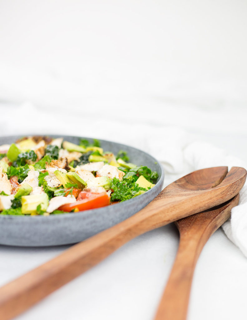 Veritcal photo of chicken salad on white background in a blue bowl with brown wooden serving spoons