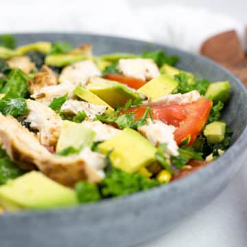 Close up of chicken salad on left with serving spoons on right, close up of chicken, avocado and tomatoes chopped in a bowl.