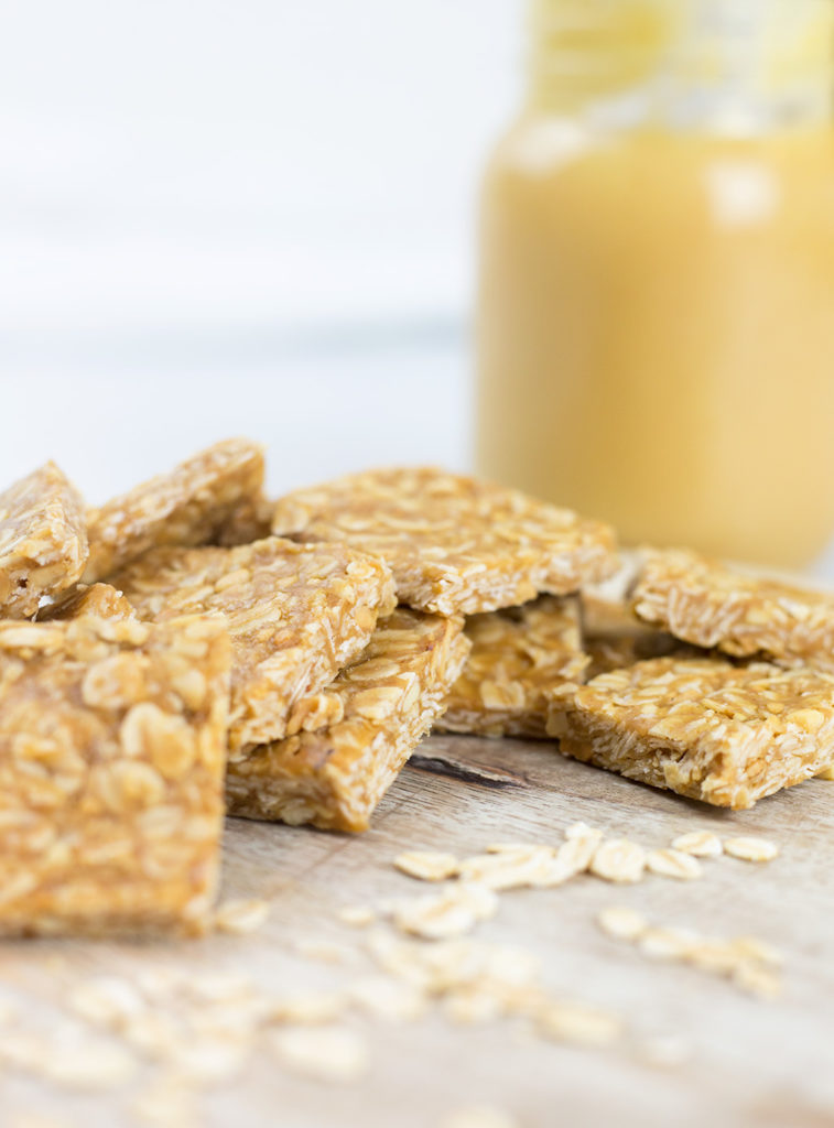 Close up vertical photo of peanut butter oat squares with jar of honey in background.