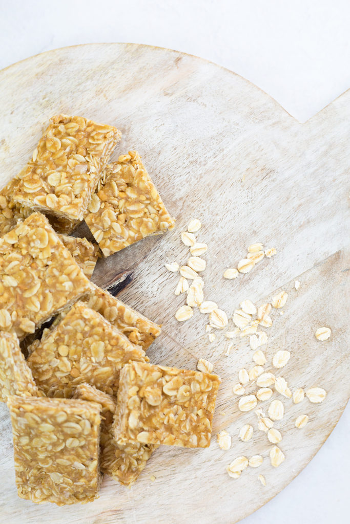 Birds eye view of peanut butter oat squares arranged on circular chopping board with a scatter of oats.