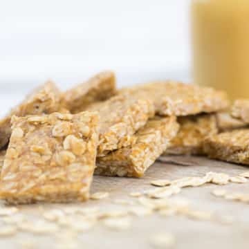 Close up of peanut butter oat squares leaning on each other on a chopping board with honey in the background.