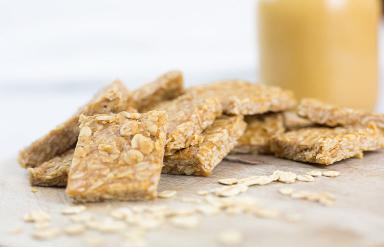 Close up of peanut butter oat squares leaning on each other on a chopping board with honey in the background.