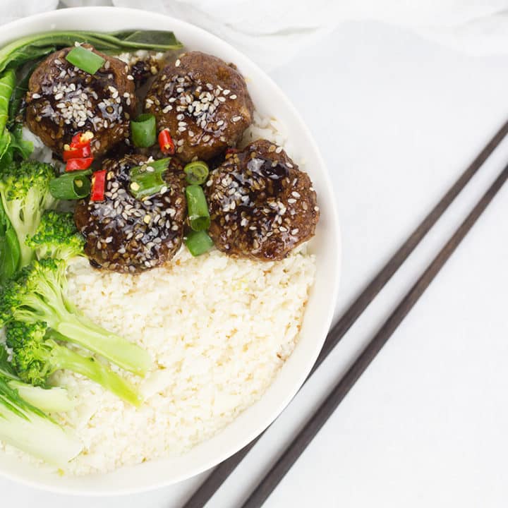 Asian meatballs and cauliflower rice with greens in a white bowl with chopsticks to the side