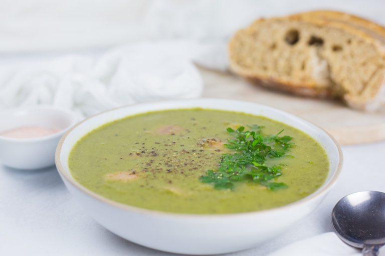 Pea and Ham Soup in a bowl with sliced bread on the side on chopping board.
