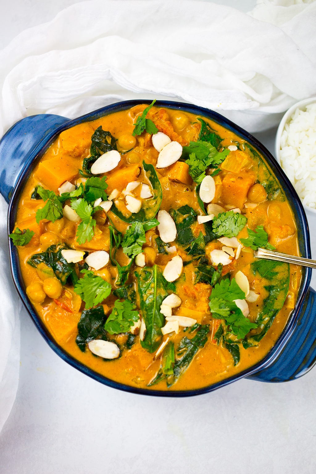 Close up of butternut squash curry in blue serving dish with white bowl of rice to the side.