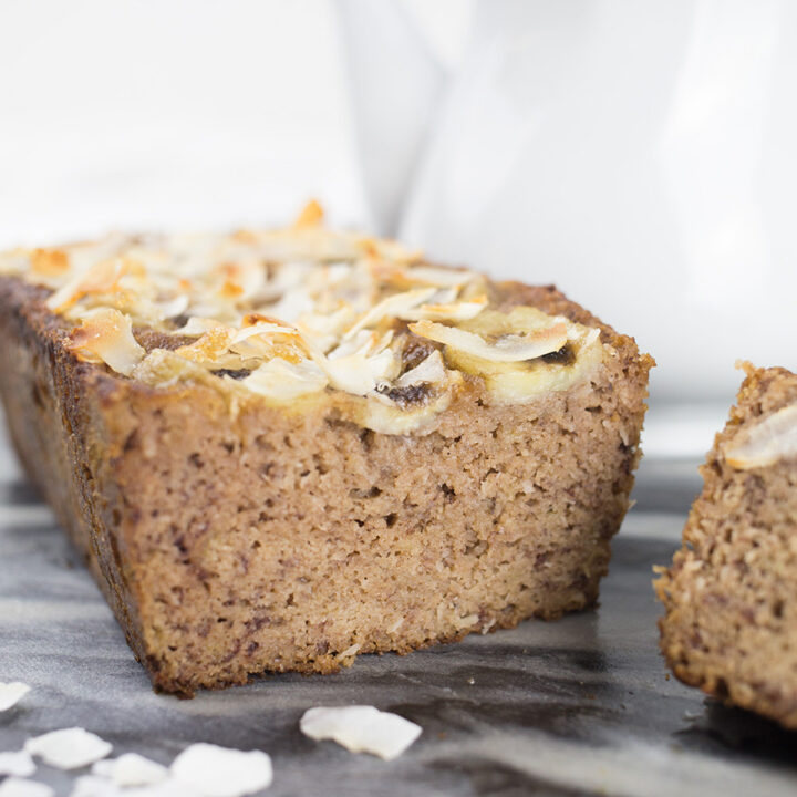 Close up of coconut banana bread slices, with shaved coconut on top and teapot behind it.