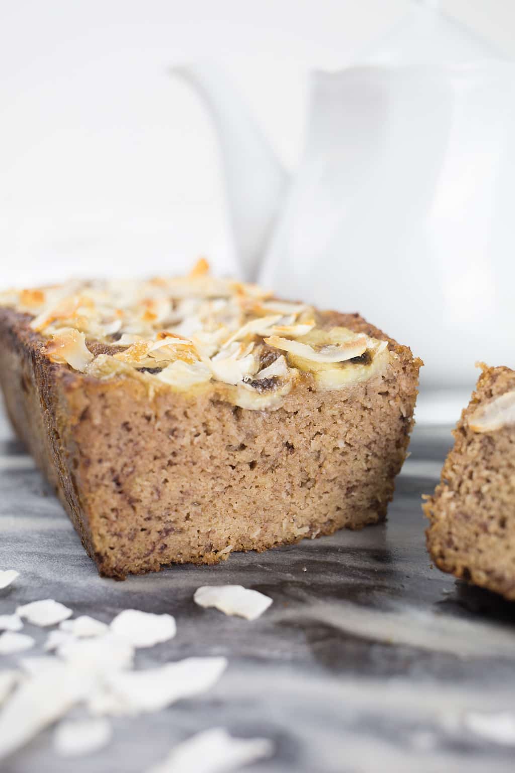 Coconut Banana Bread up close and sliced with teapot in background.